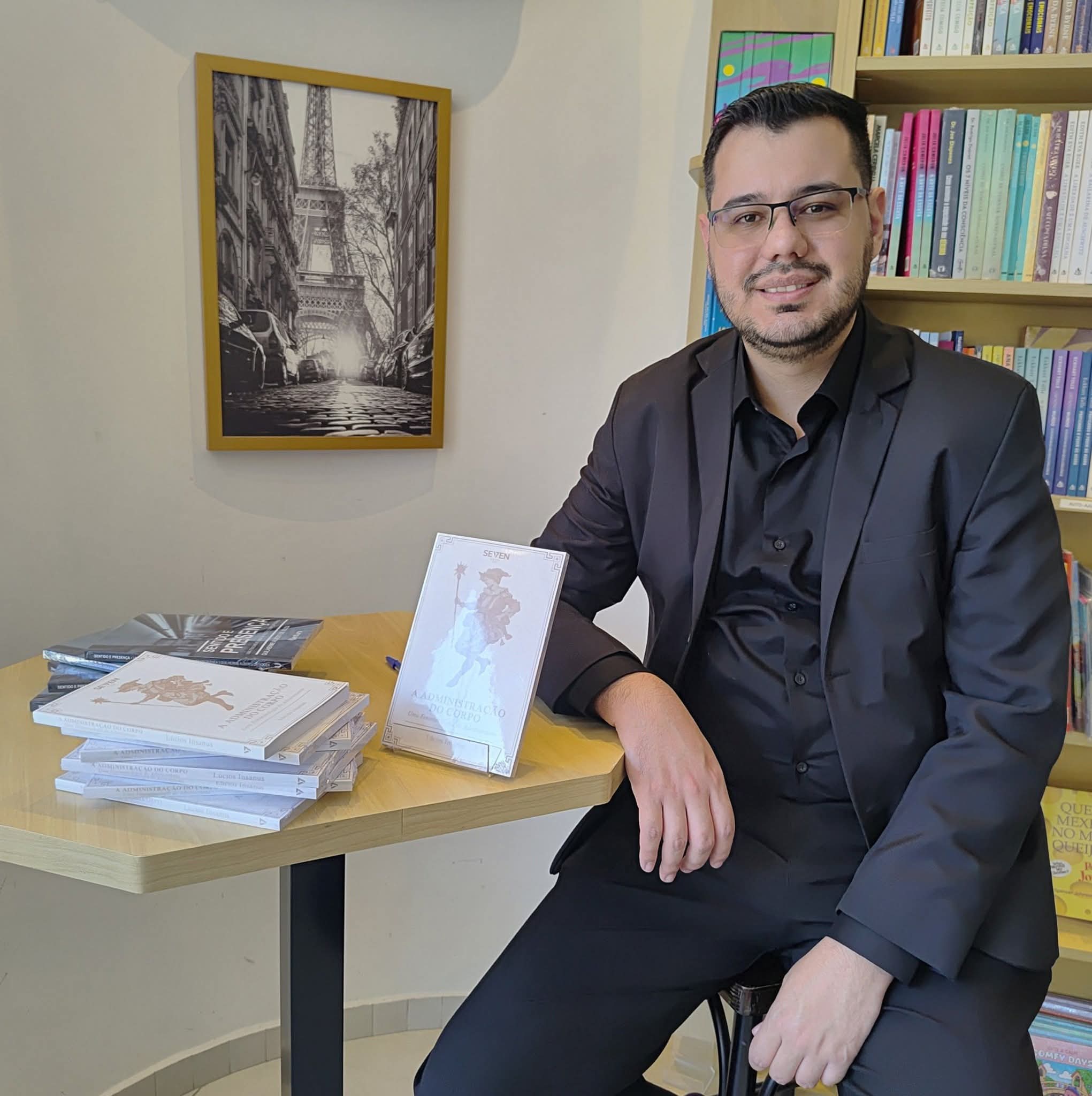 Guilherme Alberti sentado em uma biblioteca, ao lado dos seus livros